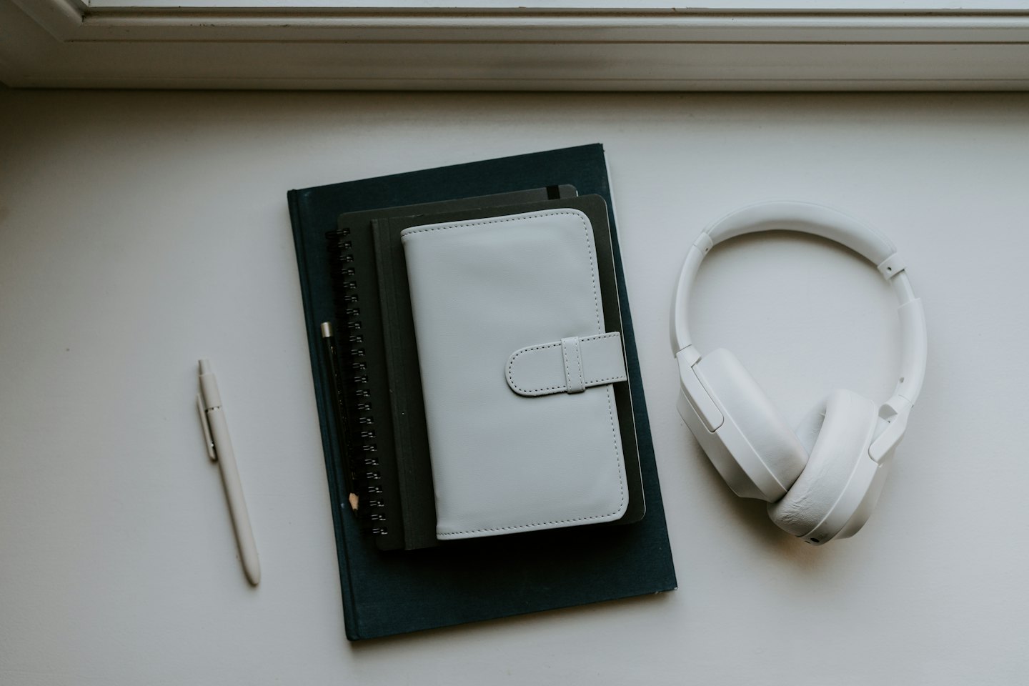 Elementos esenciales de escritorio, como cuadernos, agenda y auriculares, sobre una superficie blanca.